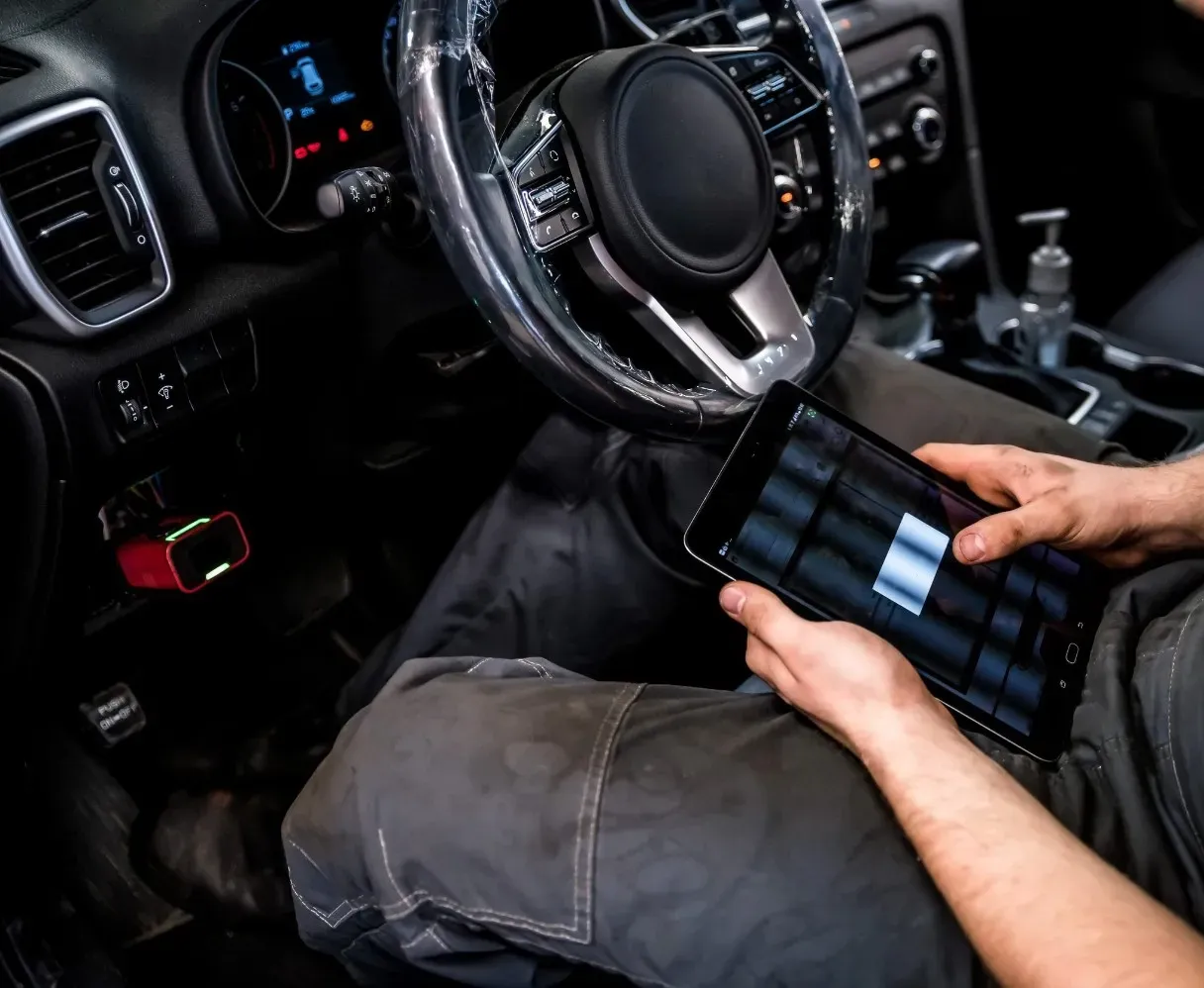 Manos sosteniendo una tableta en el interior de un automóvil, cerca del volante y el tablero.