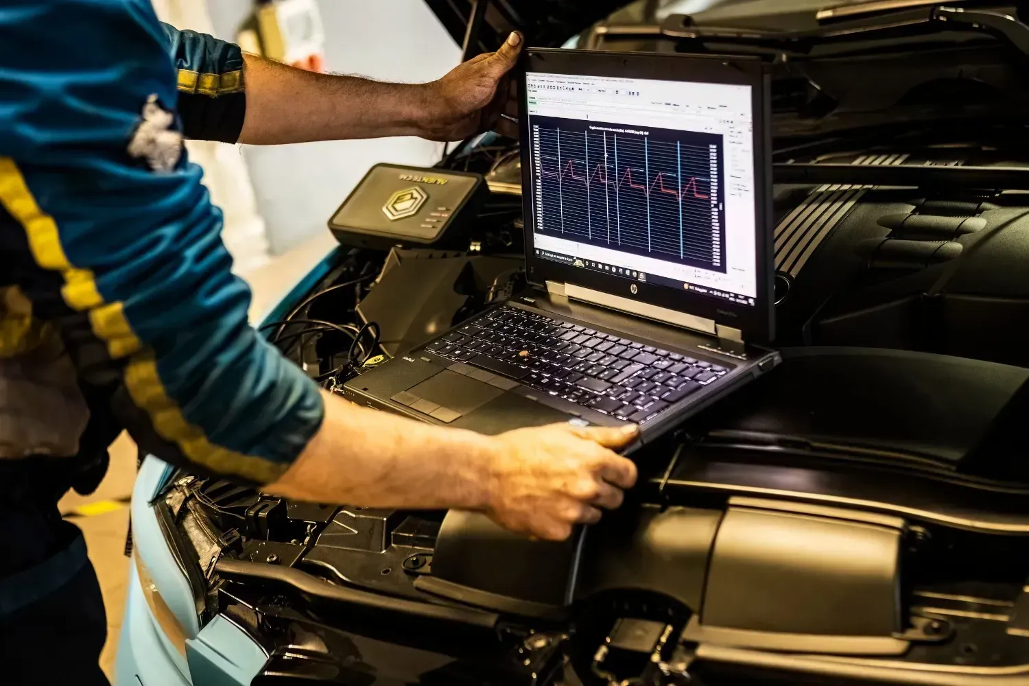 Mecánico utilizando un ordenador portátil para diagnosticar el motor de un coche en un taller.