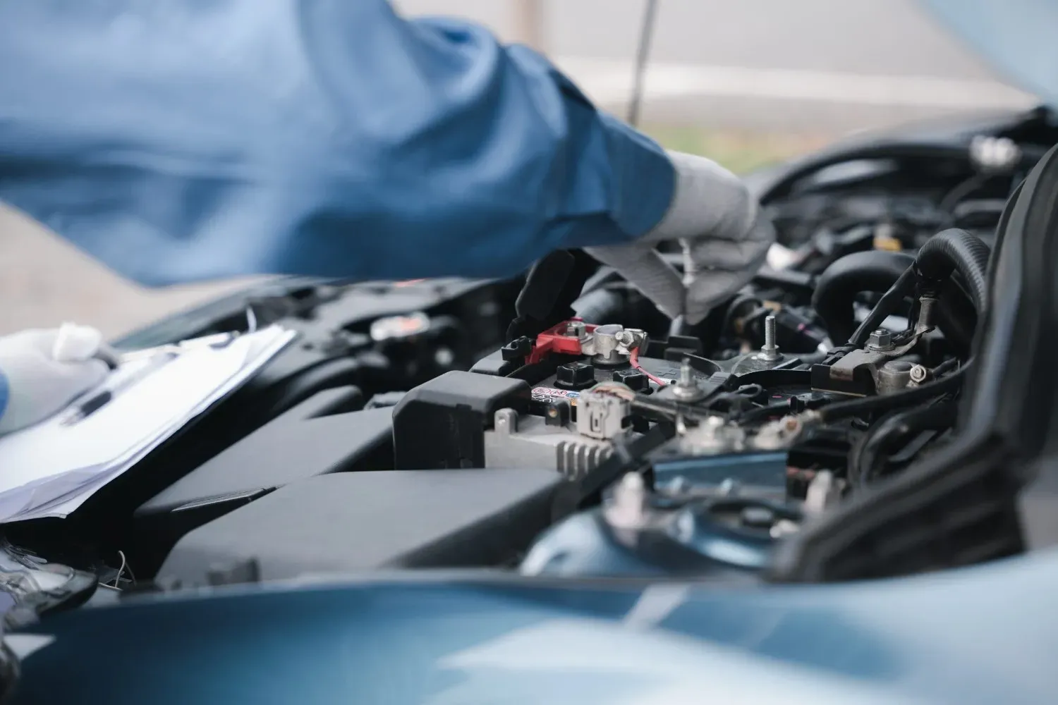 Manos enguantadas de un mecánico inspeccionando el motor de un coche bajo el capó.