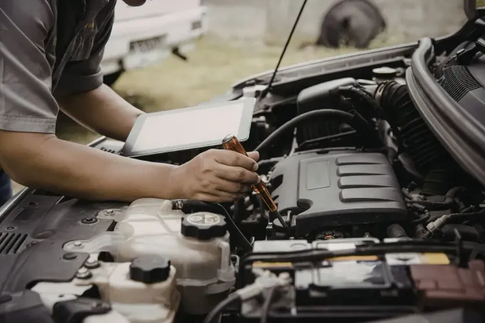Persona trabajando bajo el capó de un coche con herramientas en un taller de reparación de automóviles.