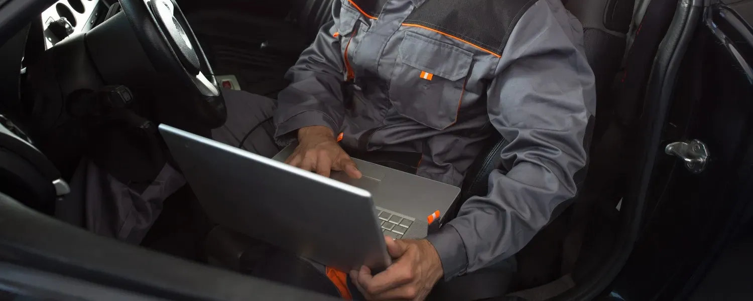 Persona con chaqueta gris usando una computadora portátil dentro del interior de un automóvil.