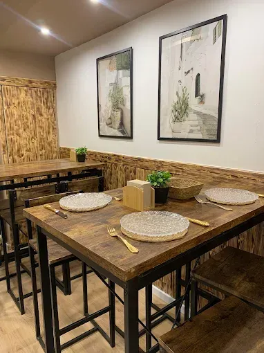 Área de comedor del restaurante: mesas de madera, sillas de metal, arte enmarcado, cubiertos.