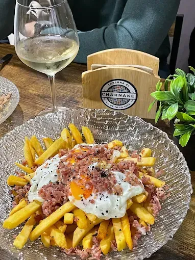 Papas fritas con huevos fritos y jamón en un plato transparente, con vino blanco y servilletero.