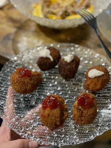 Seis bolas fritas en un plato transparente con textura, algunas con salsa. Otro plato al fondo.
