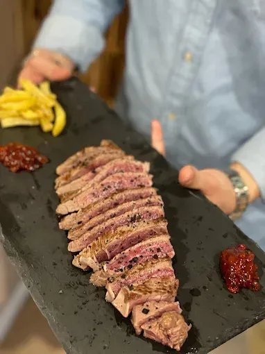 Filete rebanado con papas fritas y salsa roja en una bandeja de servir negra sostenida por una persona.