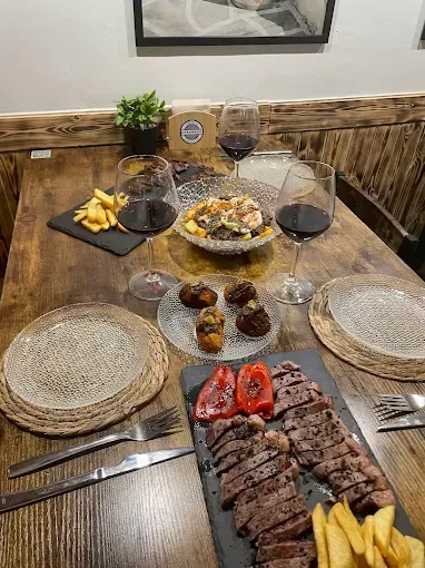 Mesa preparada para comer con bistec, papas fritas, aperitivos y copas de vino. Mesa de madera con dos cubiertos.