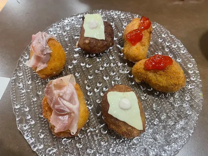 Aperitivos variados en plato de cristal: croquetas fritas con carne, queso o salsa roja.