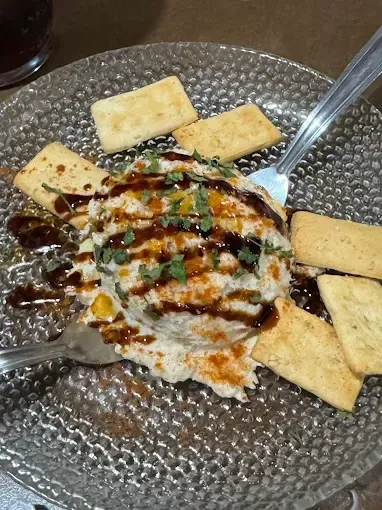 Dip cremoso cubierto con llovizna y hierbas, servido con galletas en un plato de vidrio texturizado con tenedores.