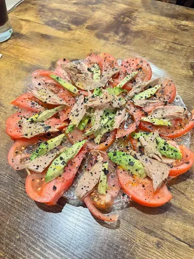 Ensalada de tomate, aguacate y atún dispuesta en un plato de vidrio, sazonada con pimienta negra.
