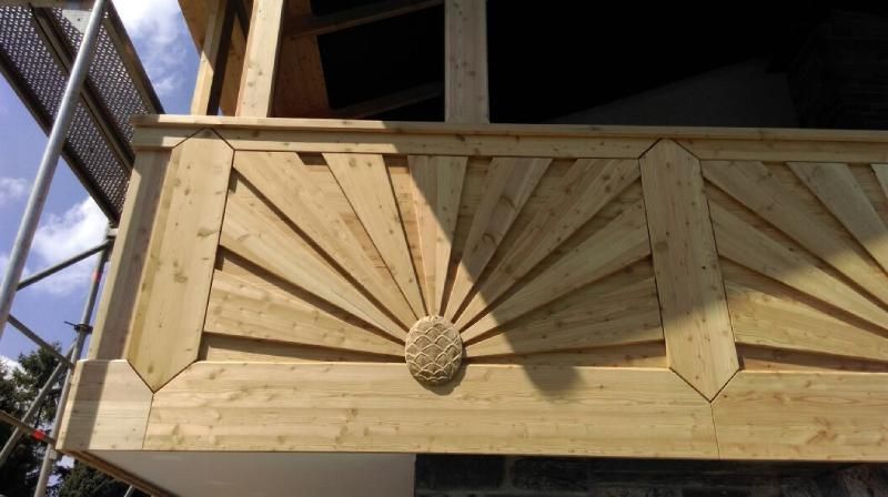 Ein hölzernes Balkongeländer mit dekorativen Sonnenmotiven und einem zentralen kreisförmigen Ornament.