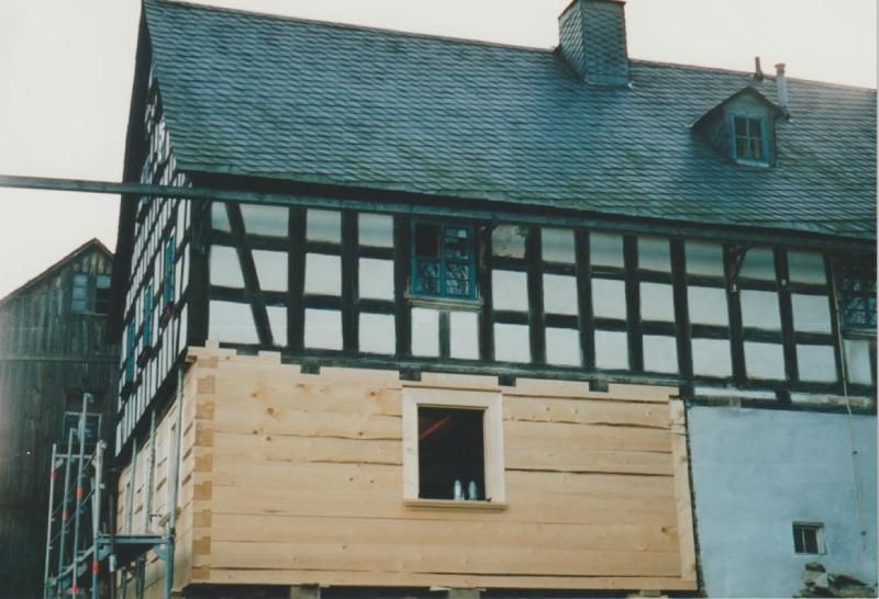 Ein historisches Fachwerkhaus, das derzeit restauriert wird und bei dem neue, helle Holzstämme an der Erdgeschosswand angebracht wurden.