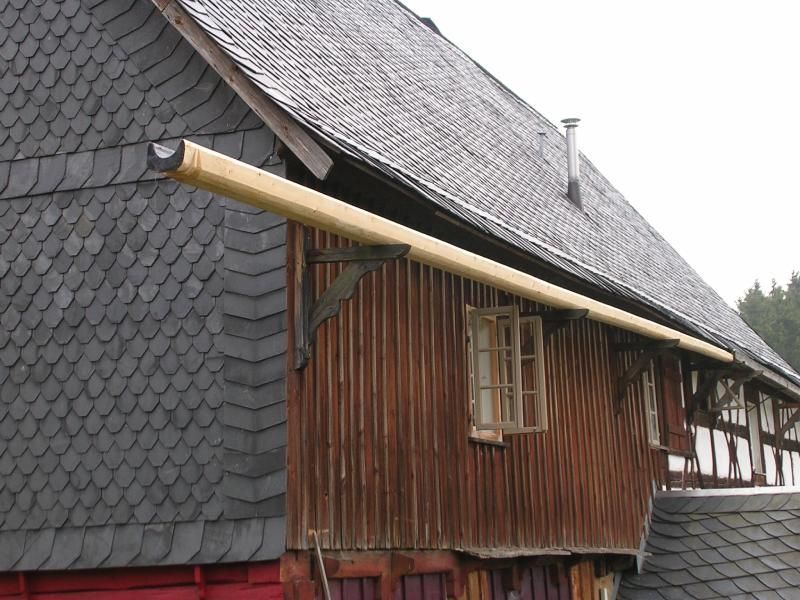 Ein Holzhaus mit einem schiefergedeckten Dach und einer langen, hellen Holzrinne, die sich von der Seitenwand nach außen erstreckt.