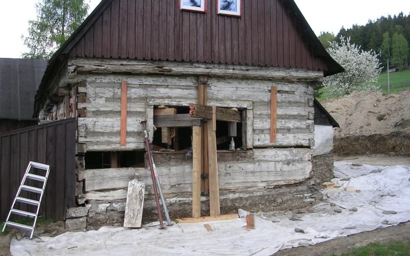 Eine alte Blockhütte, deren Außenwände mithilfe von Stützbalken und Hebern auf einer Baustelle repariert werden.