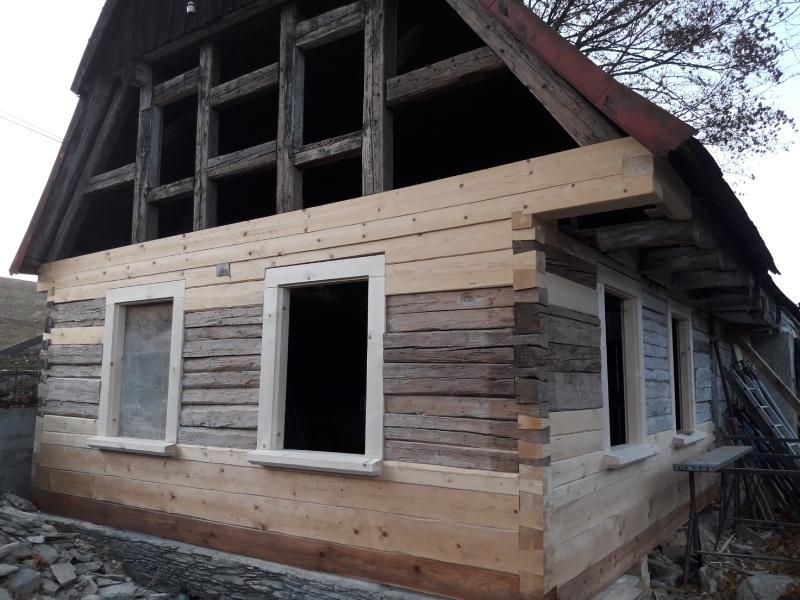 Ein rustikales Fachwerkhaus, das derzeit renoviert wird und eine Mischung aus neuen hellen Holzplanken und verwitterten grauen Balken aufweist.