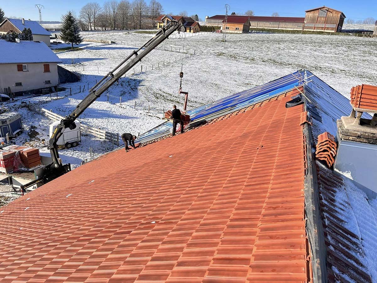 Deux ouvriers sur un toit qui posent des tuiles à l'aide d'un camion-grue