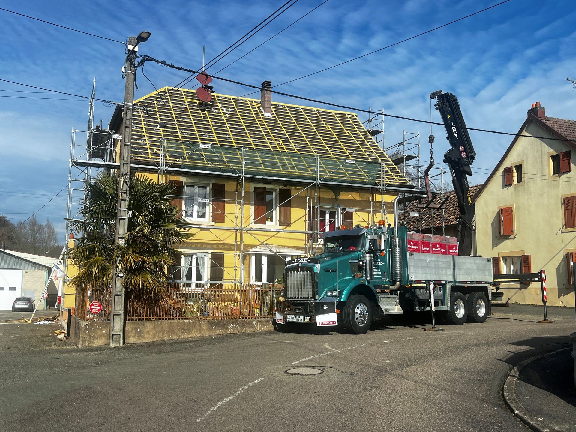 Camion-grue devant une maison à la façade jaune