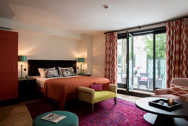 Ein Hotelzimmer mit Kingsize-Bett, Sessel, Ottomane, Couchtisch und Balkon.