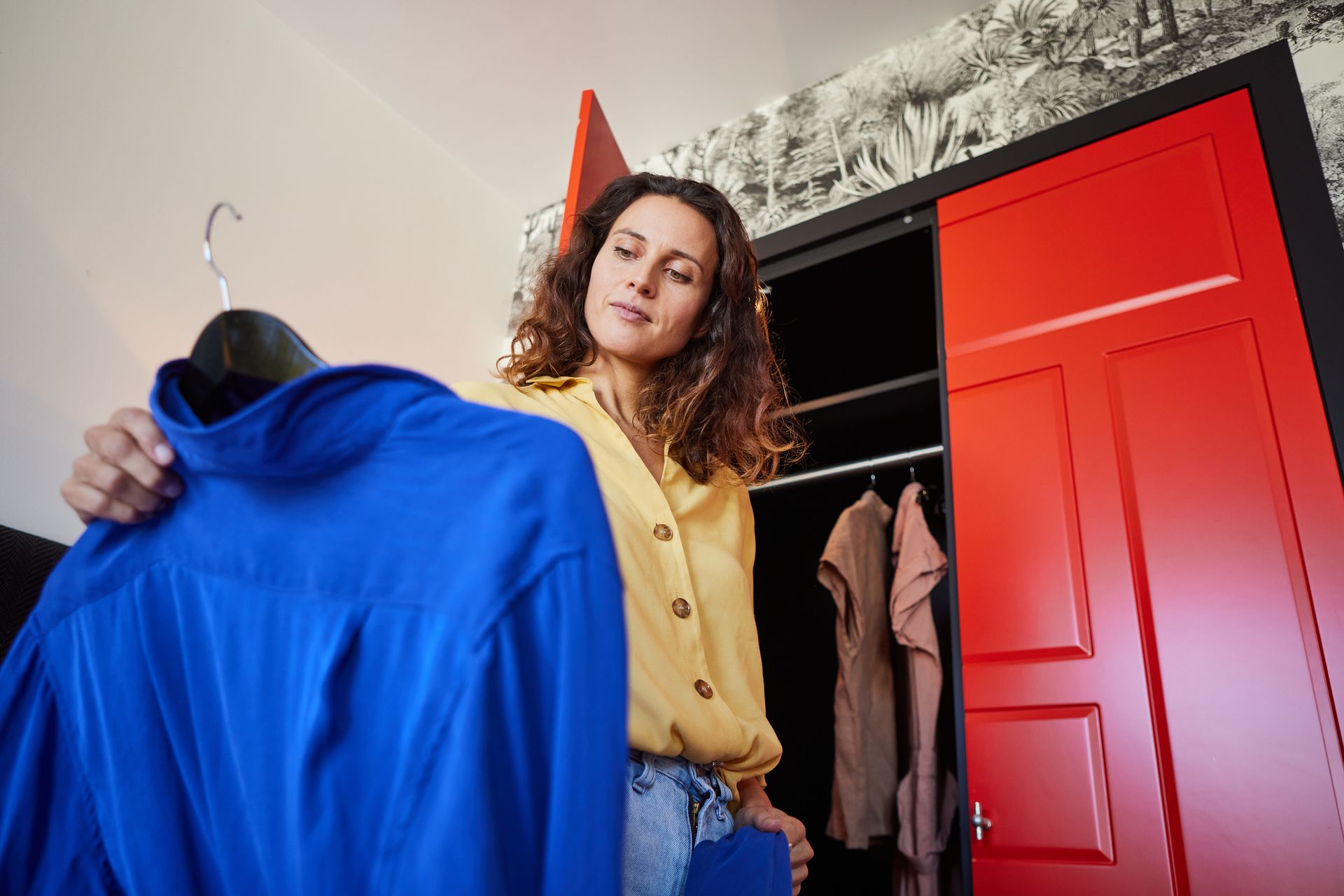 Eine Frau in einem blauen Overall sitzt auf einem Stuhl und hält ein Tablet in der Hand.