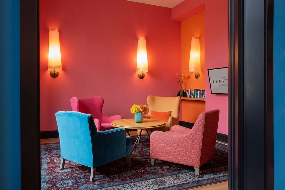 Ein Raum mit rosa Wänden und bunten Stühlen und einem Tisch.