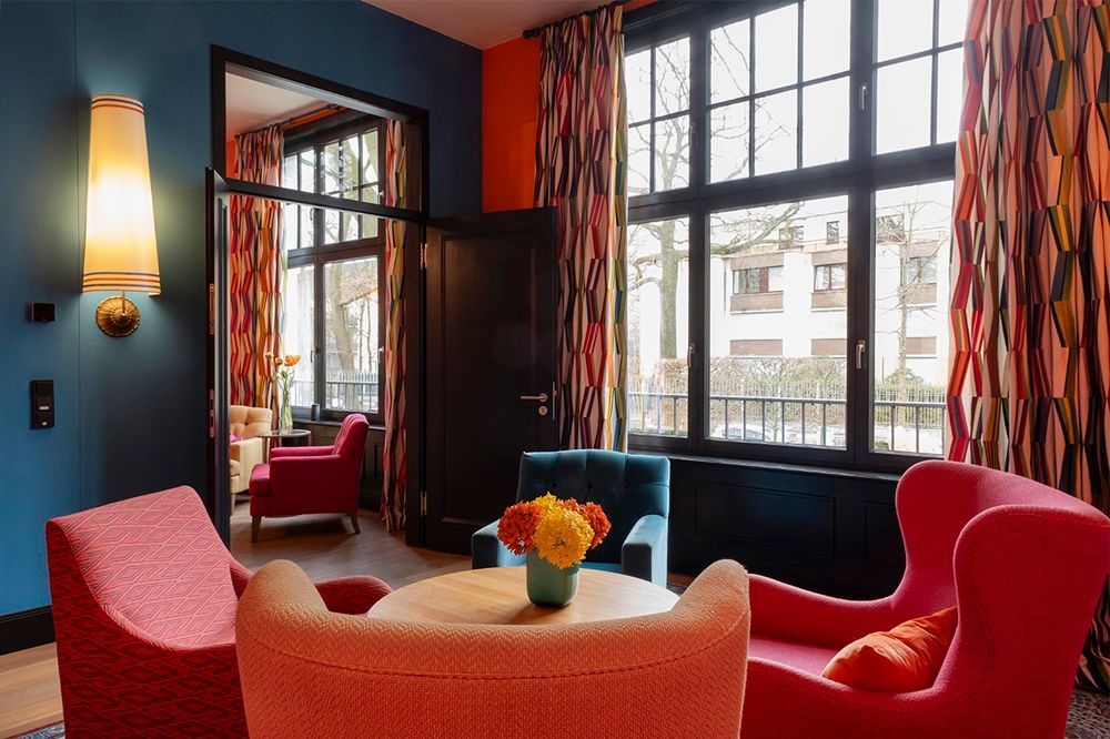 Ein Wohnzimmer mit bunten Stühlen und einem Tisch mit einer Vase mit Blumen darauf.