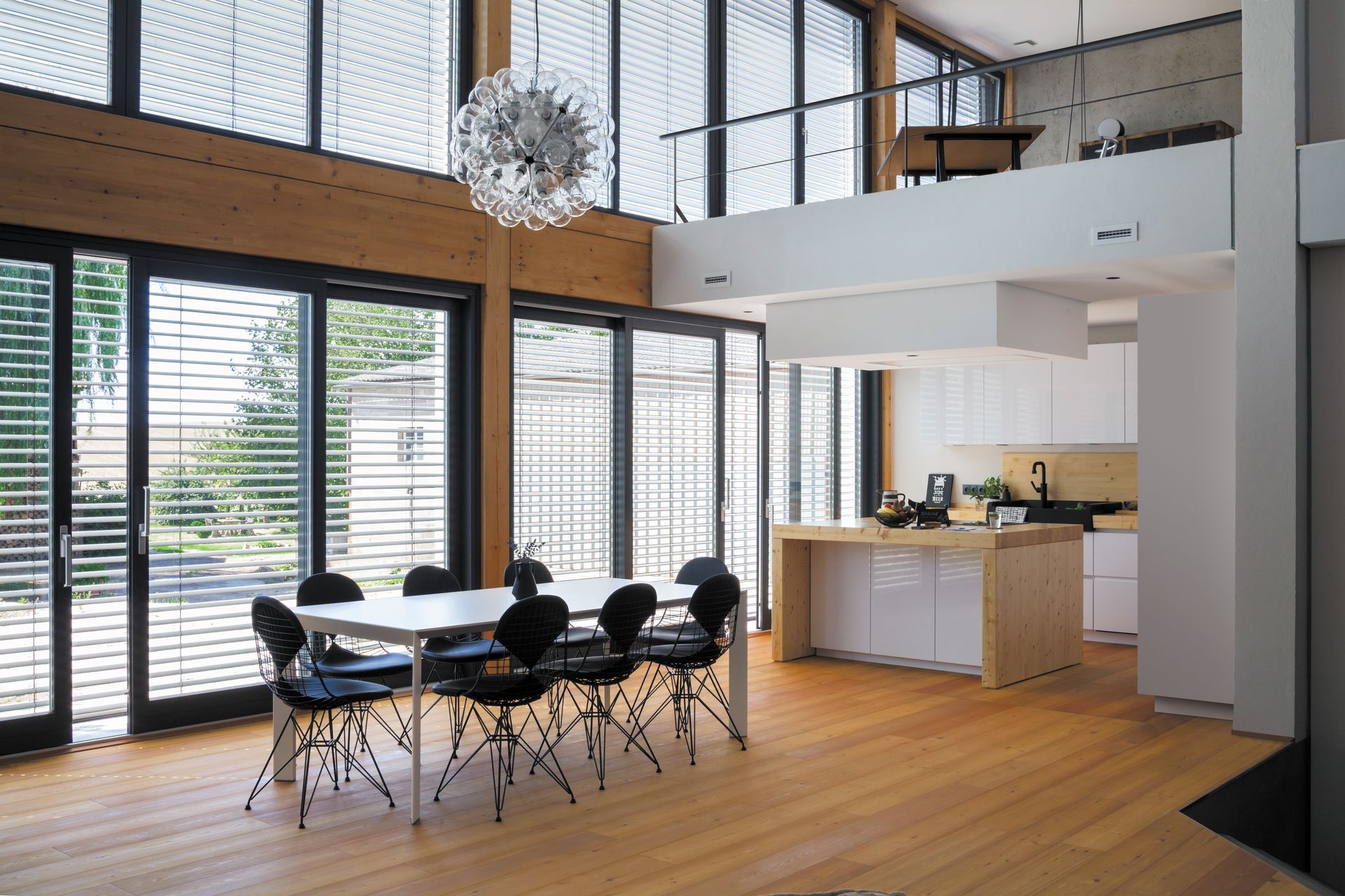 Une salle à manger et une cuisine modernes et ouvertes, avec des baies vitrées, un parquet et une mezzanine.