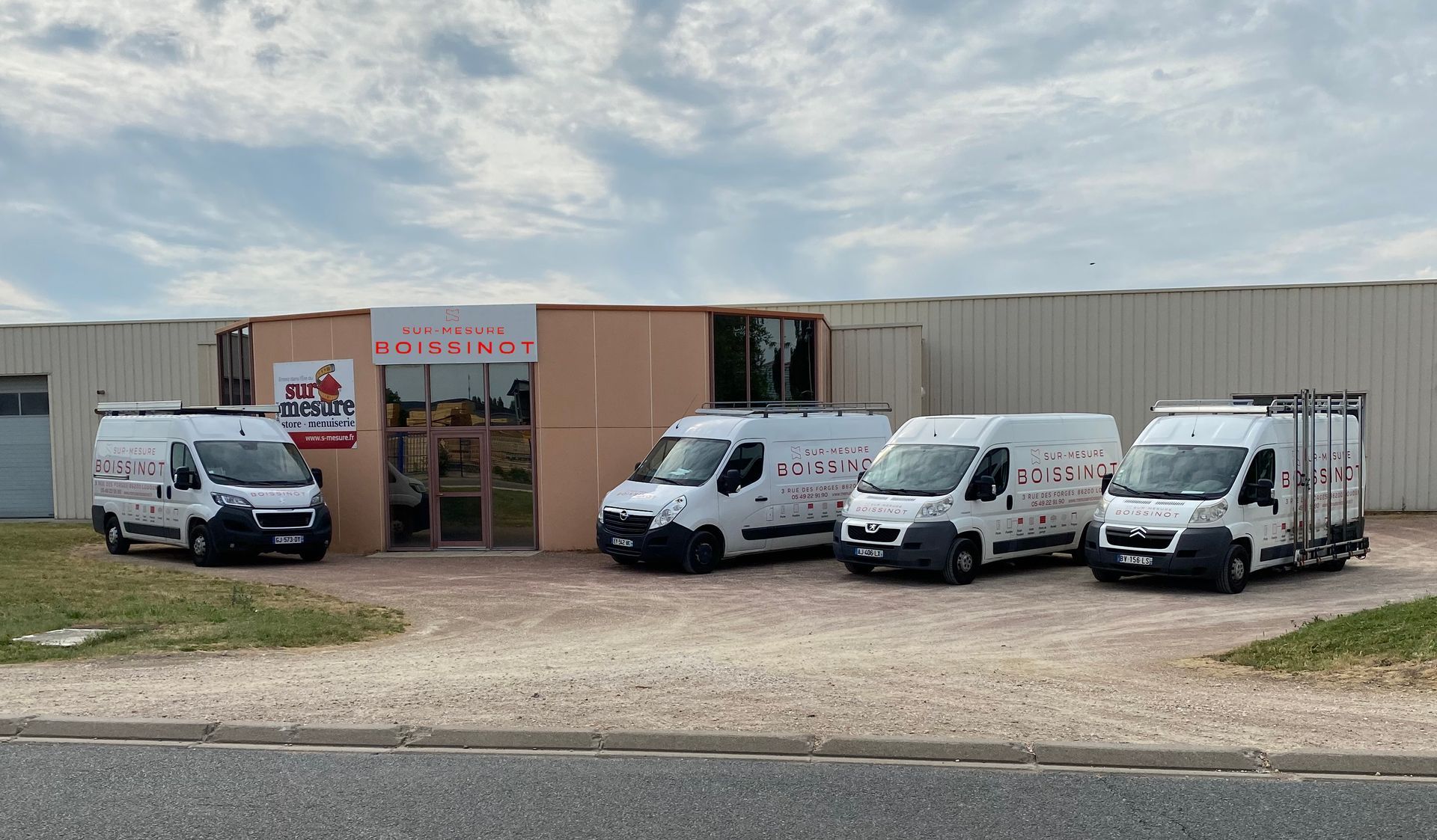 Quatre fourgonnettes de service blanches stationnées devant un bâtiment commercial avec une enseigne affichant le nom de l'entreprise « Miroiterie ».