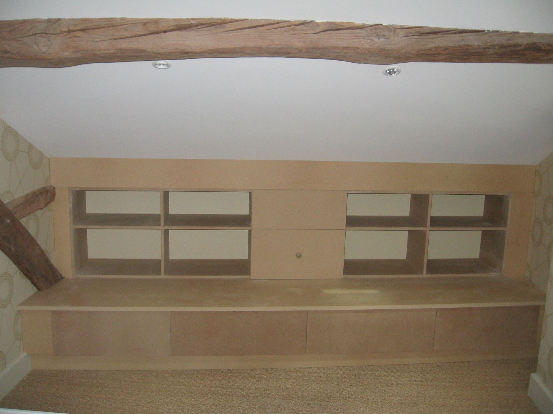 Étagères et meubles bas en MDF sur mesure, installés sous un plafond incliné dans une pièce avec une poutre de toit en bois.