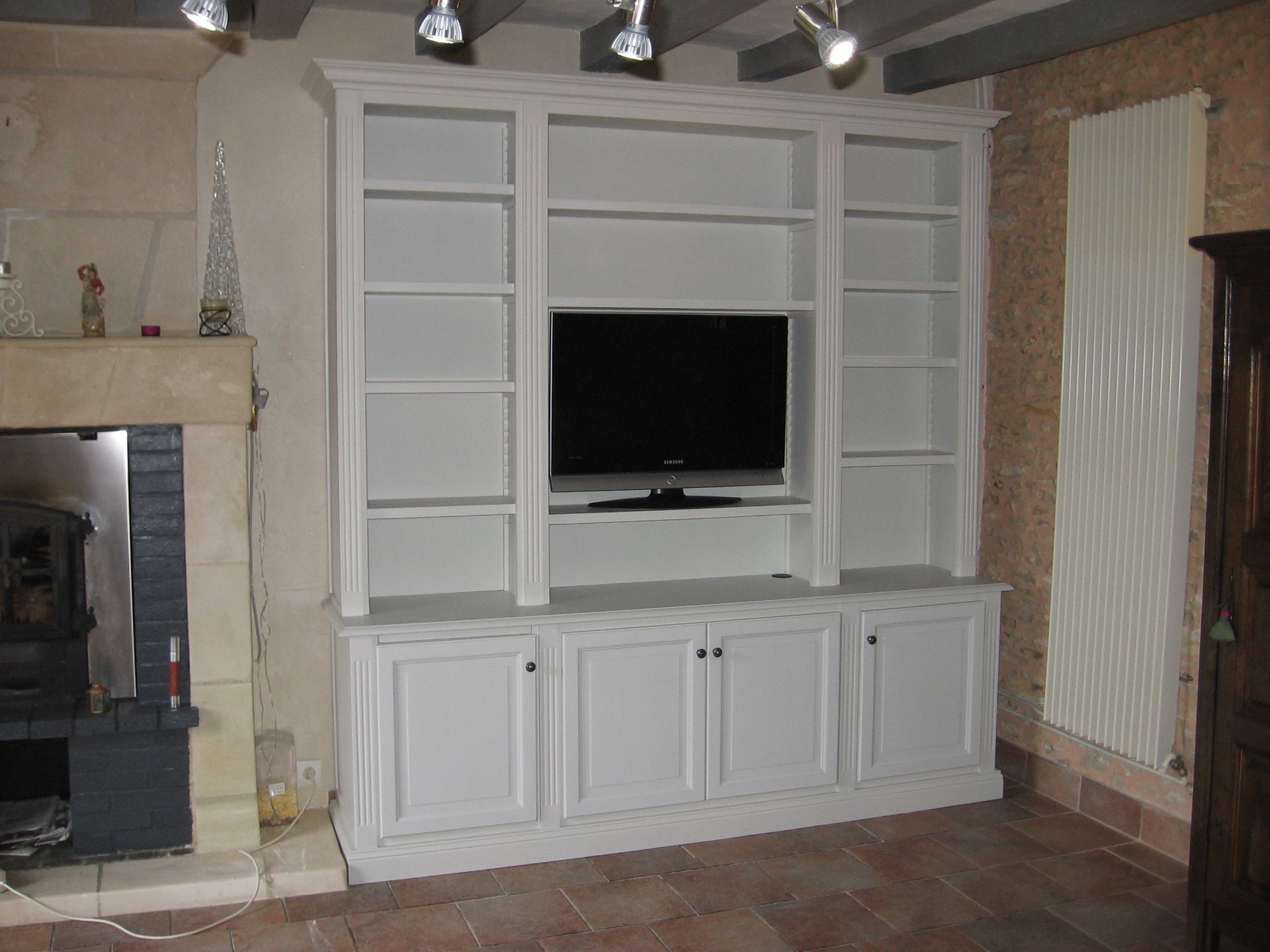 Meuble mural blanc sur mesure avec télévision centrale, étagères ouvertes et meubles bas dans une pièce avec cheminée en pierre.