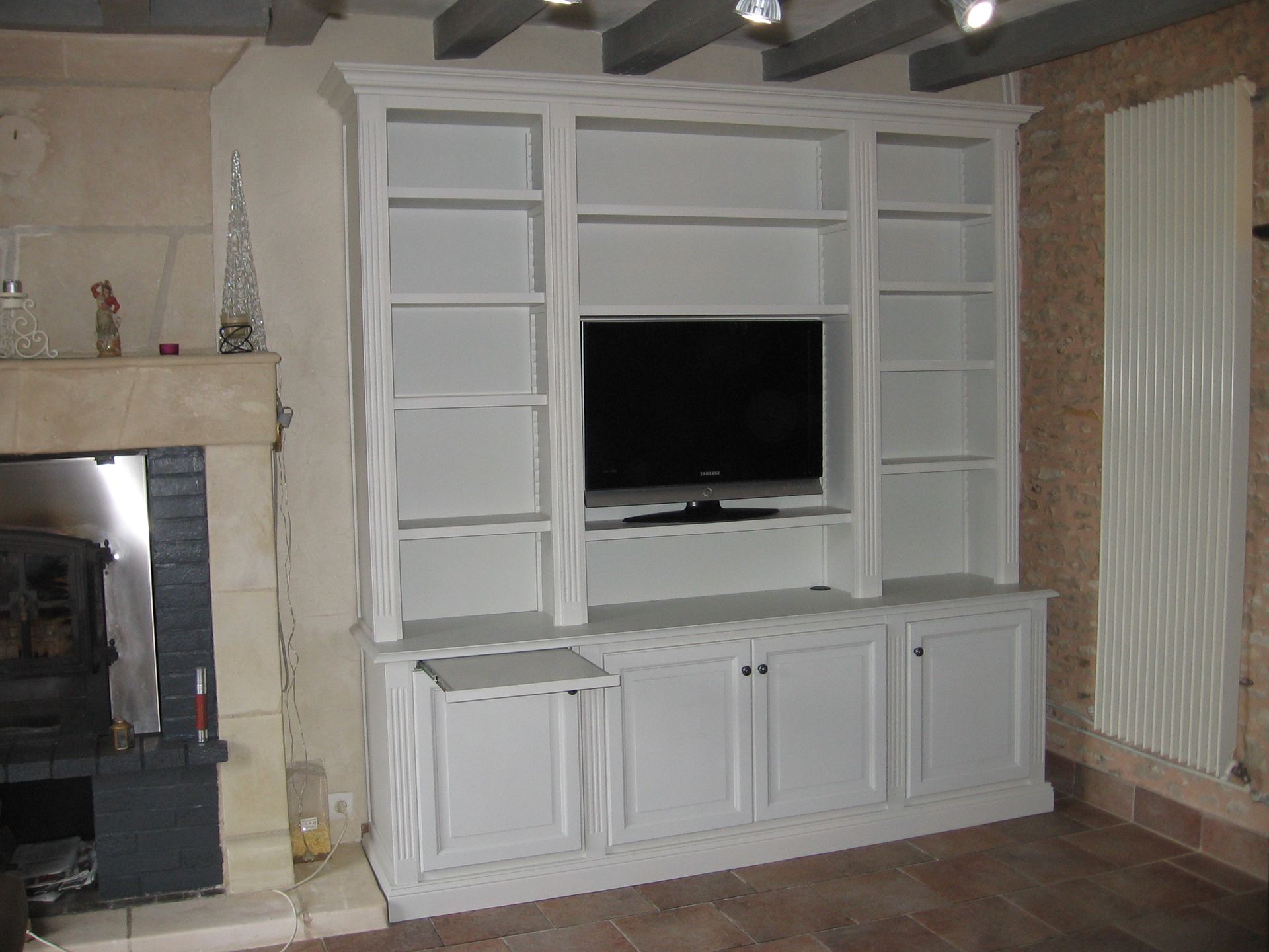 Un meuble mural blanc intégré avec des étagères ouvertes, une télévision centrale et des rangements bas dans une pièce rustique.