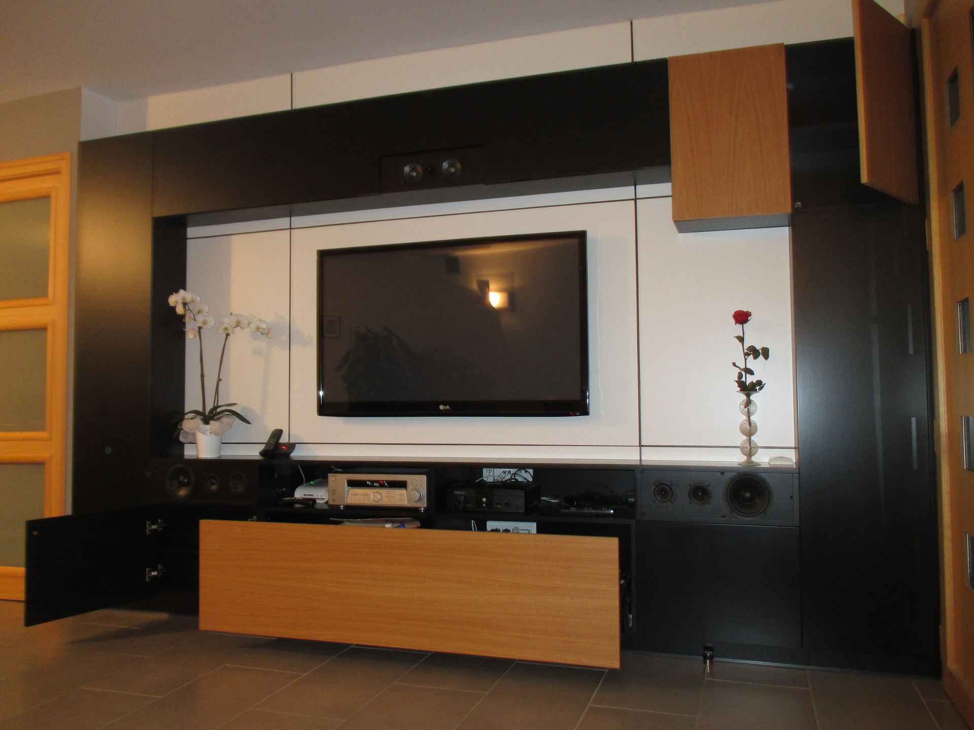 Ce meuble multimédia moderne en noir et blanc comprend un téléviseur central, des portes en bois clair et des haut-parleurs intégrés.