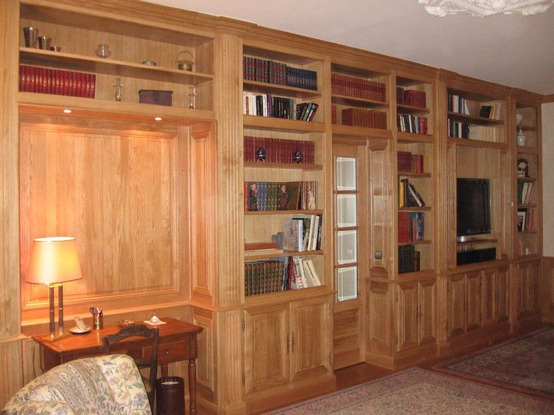 Une grande bibliothèque en chêne, s'étendant du sol au plafond, occupe tout un mur et comprend un éclairage intégré, un espace bureau et une télévision à écran plat.