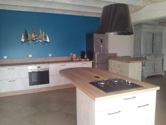 Une cuisine moderne avec des armoires blanches, un îlot central en bois avec une plaque de cuisson et un mur bleu céruléen.