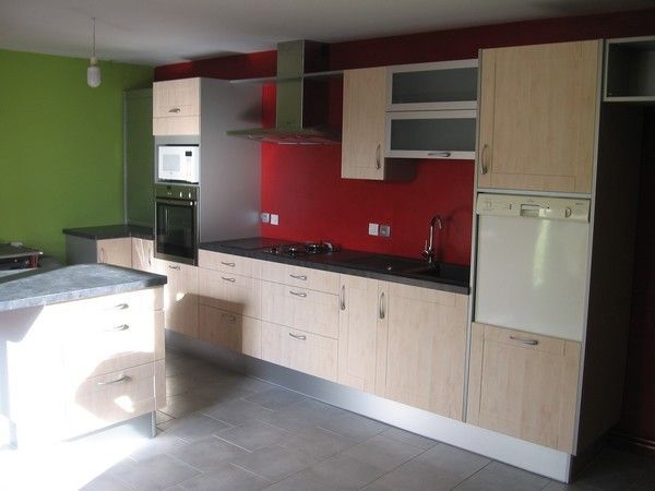 Une cuisine moderne avec des armoires en bois clair, un comptoir noir, une crédence rouge et un mur vert.