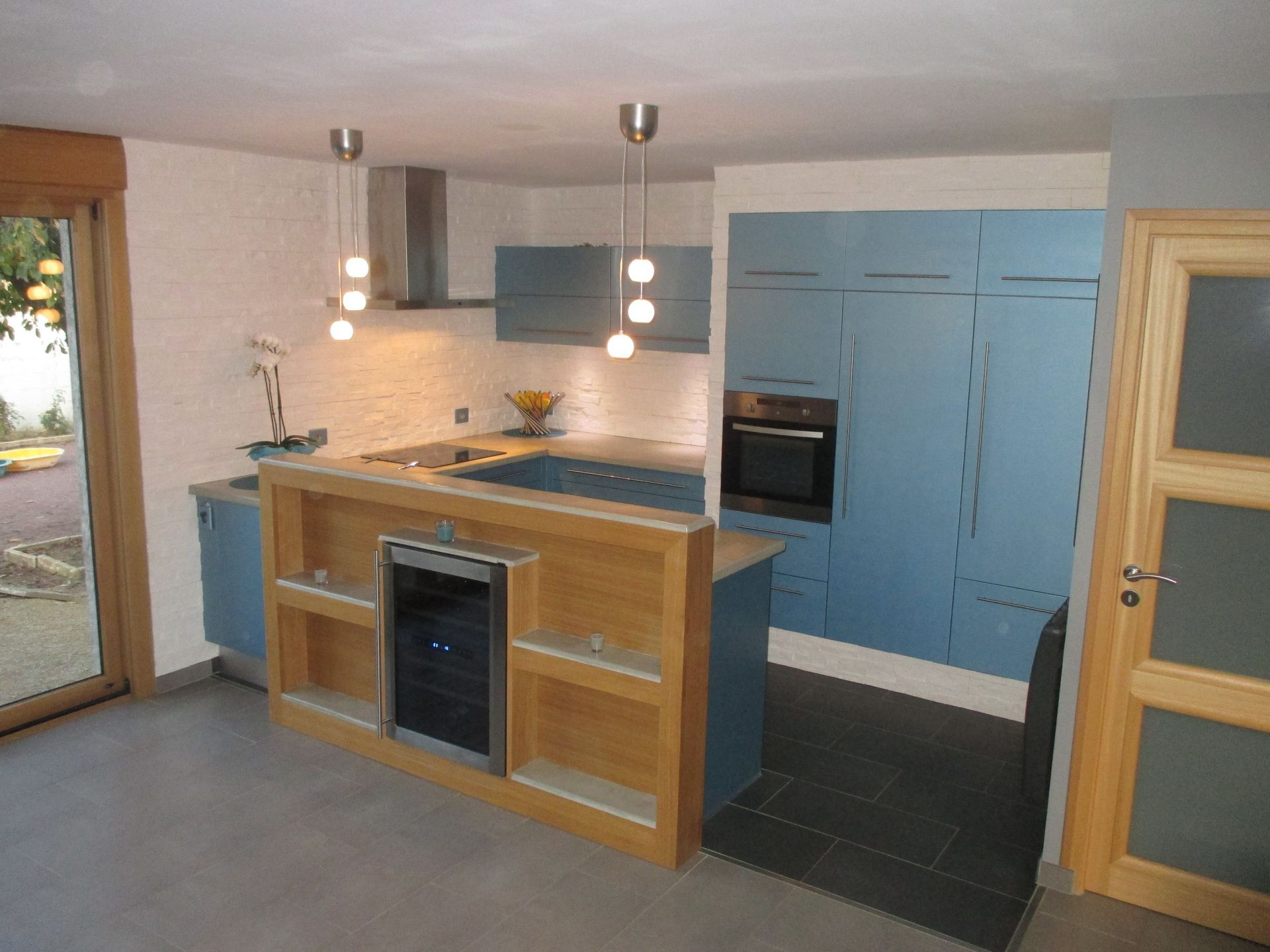 Une cuisine moderne avec des armoires bleues, des touches de bois clair, un four intégré et un îlot central avec étagères.