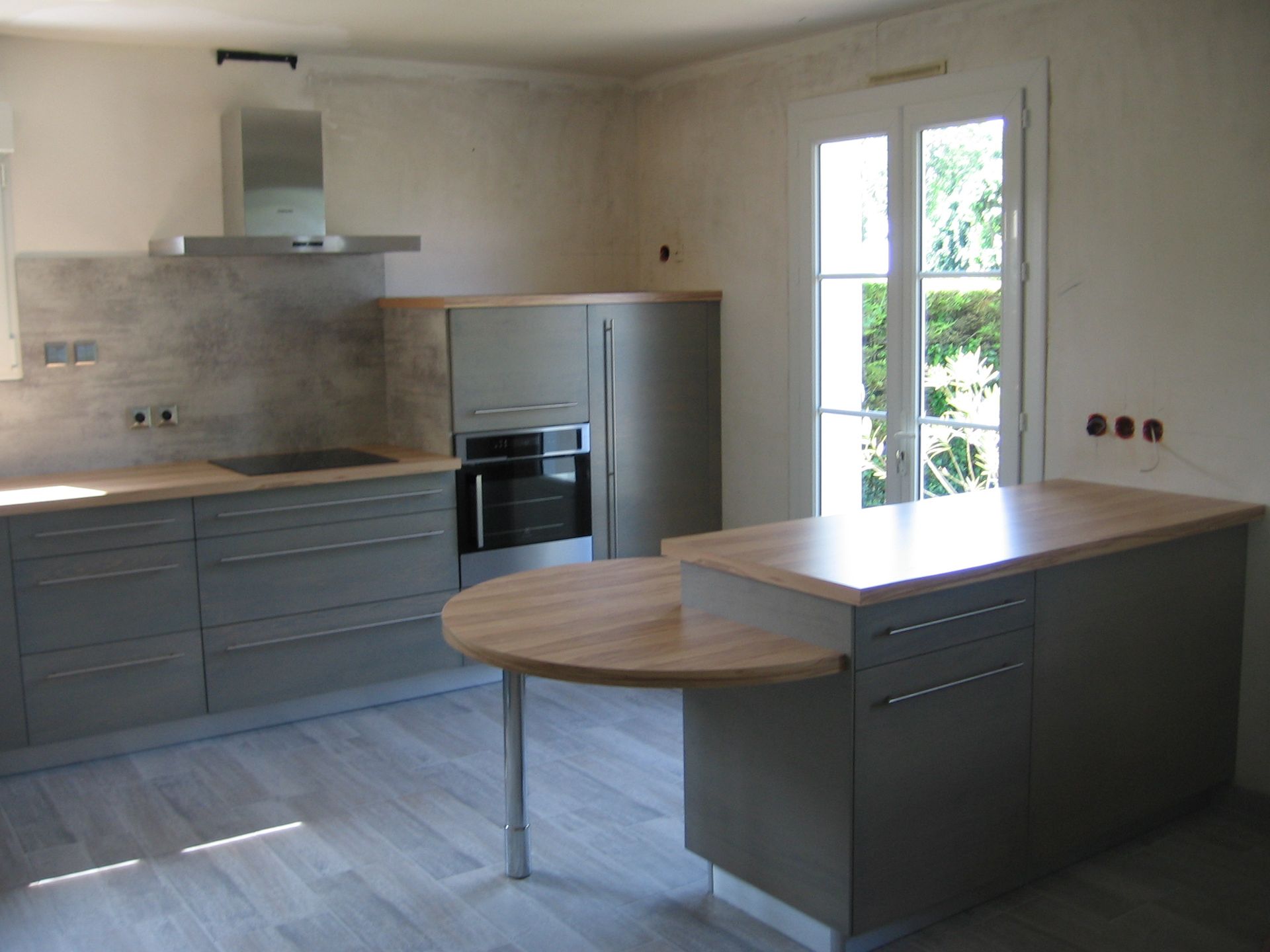 Une cuisine moderne avec des placards gris, un plan de travail en bois, un bar pour le petit-déjeuner et une porte-fenêtre donnant sur l'extérieur.