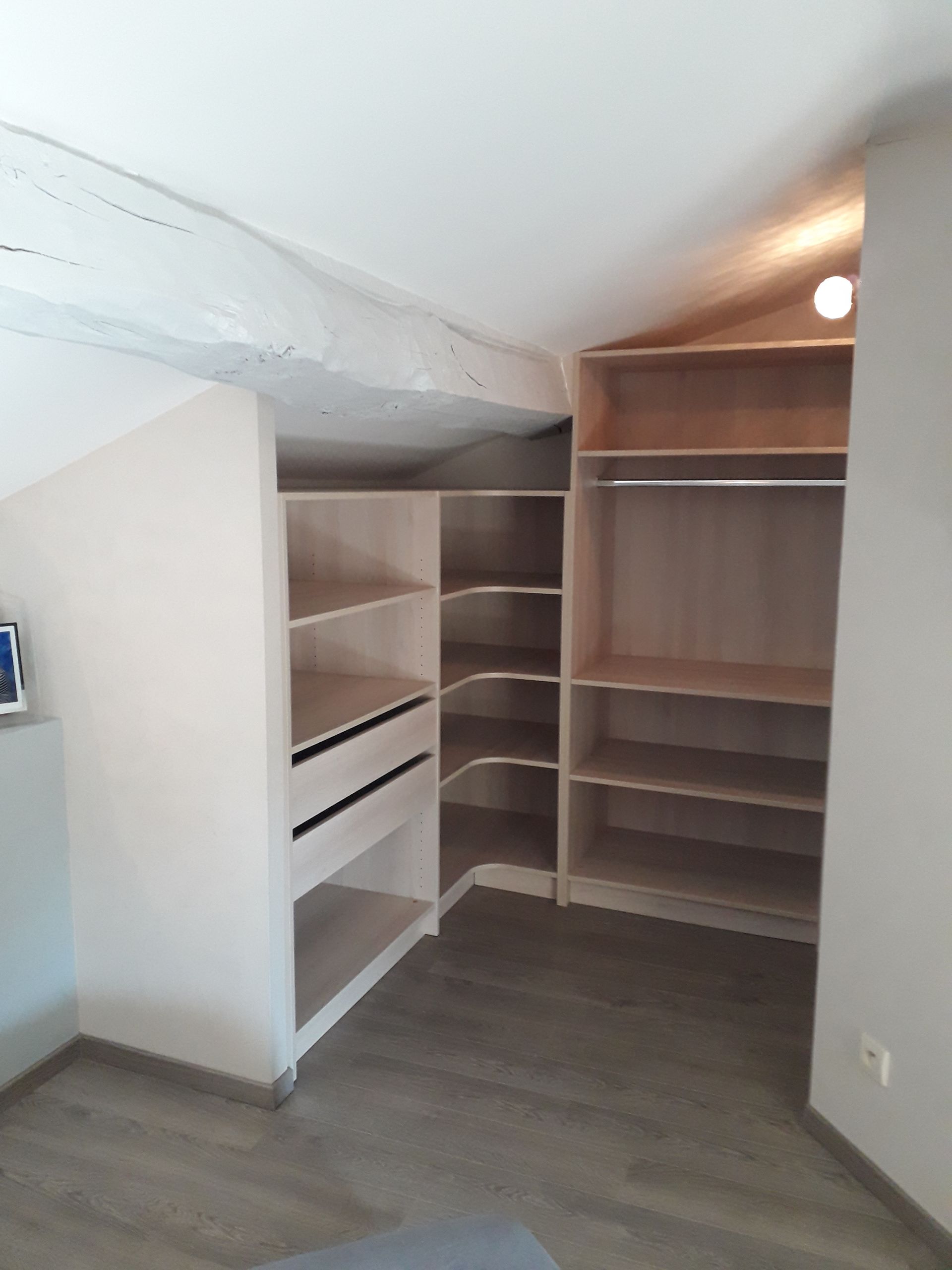 Une étagère encastrée sur mesure en bois clair avec espace de penderie, installée dans une pièce mansardée avec plafond en pente.