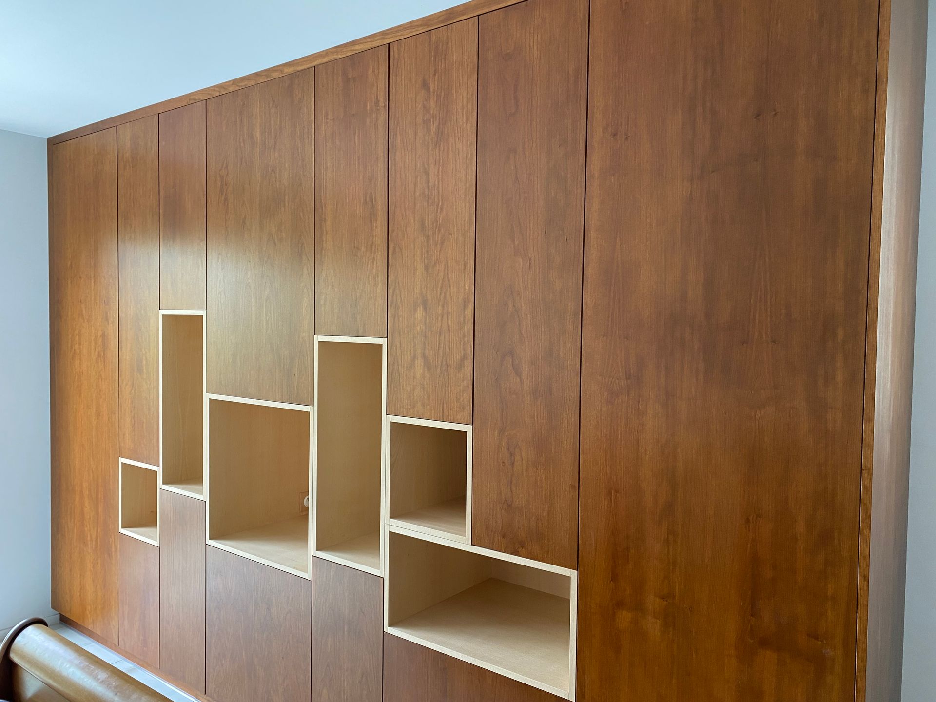 Une grande armoire murale en bois sur mesure, comportant une série de découpes rectangulaires claires servant d'étagères ouvertes.