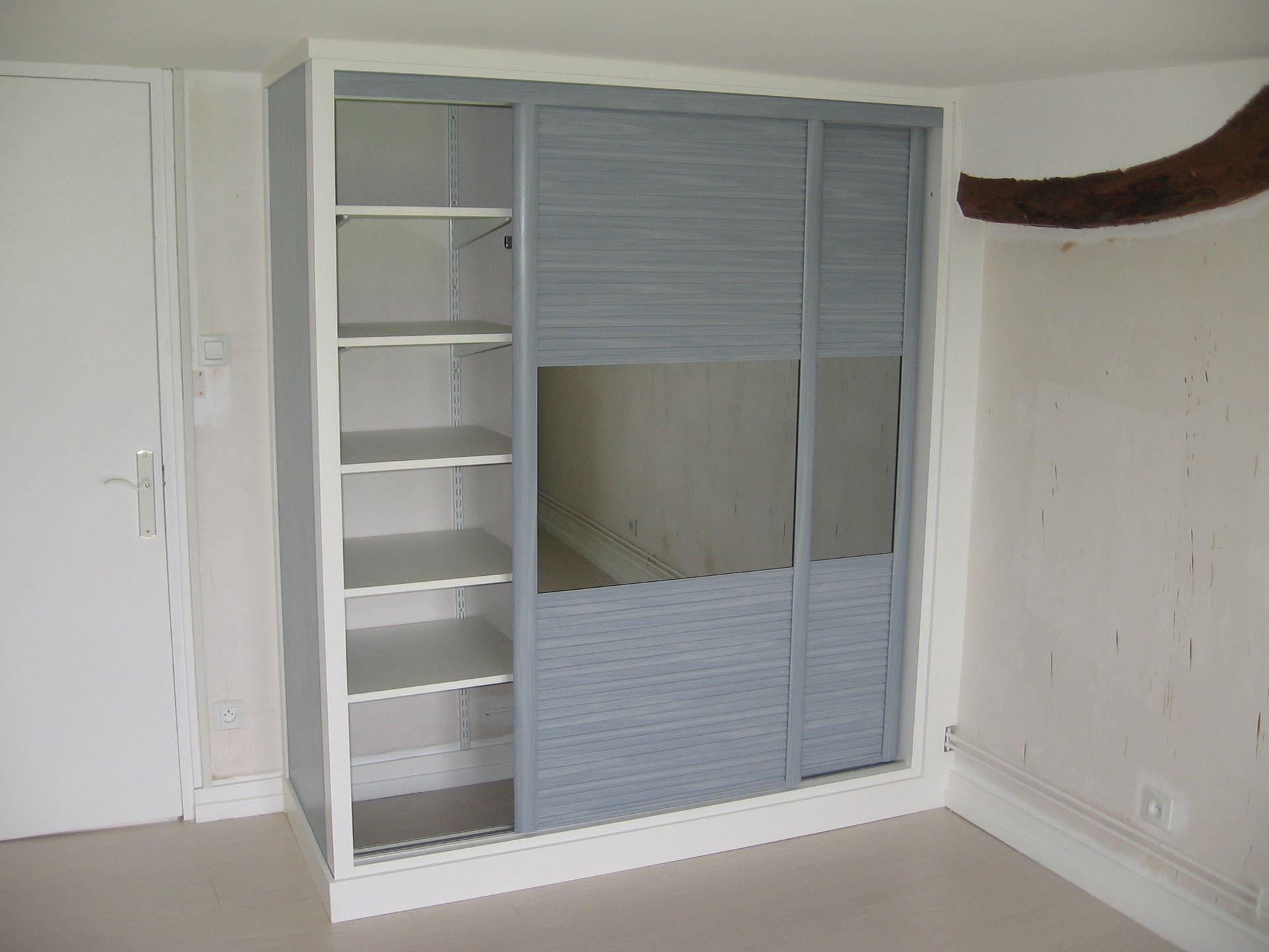 Un placard à cadre blanc avec des étagères ouvertes à gauche et un panneau de porte coulissante comportant un segment de miroir à droite.