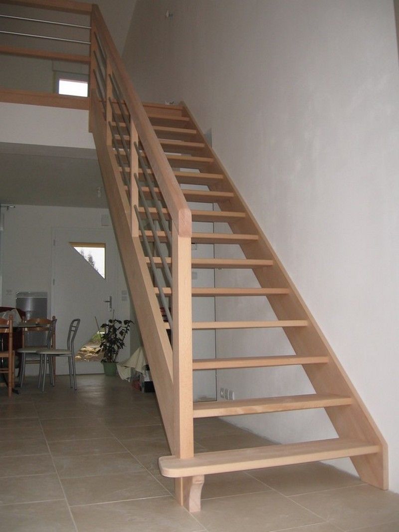 Un escalier en bois avec contremarches ouvertes et balustres métalliques mène à un niveau supérieur dans un espace intérieur lumineux et moderne.