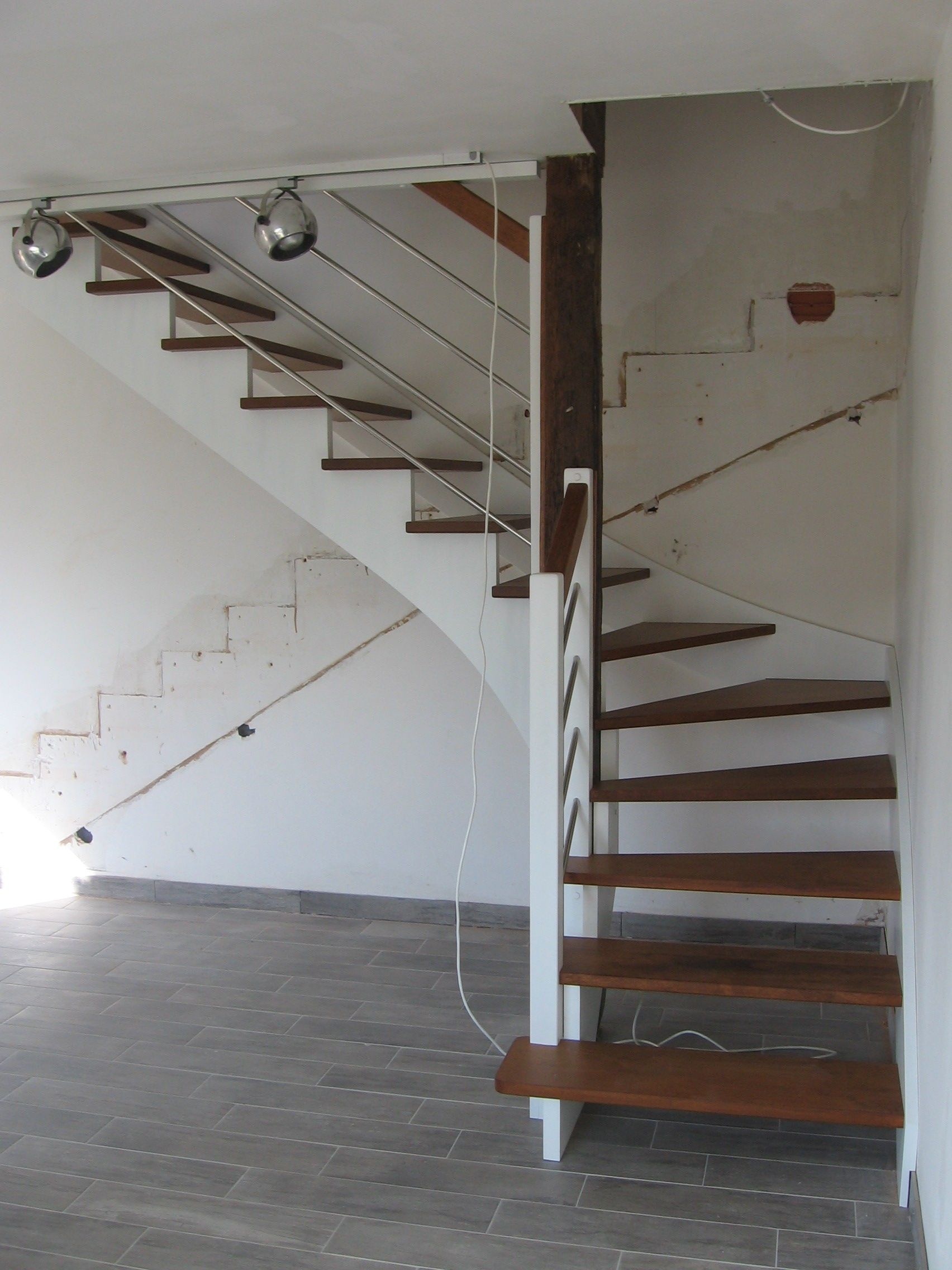 Un escalier moderne avec des marches en bois et une structure en métal blanc, doté de fines rampes à câbles verticaux, dans une pièce.