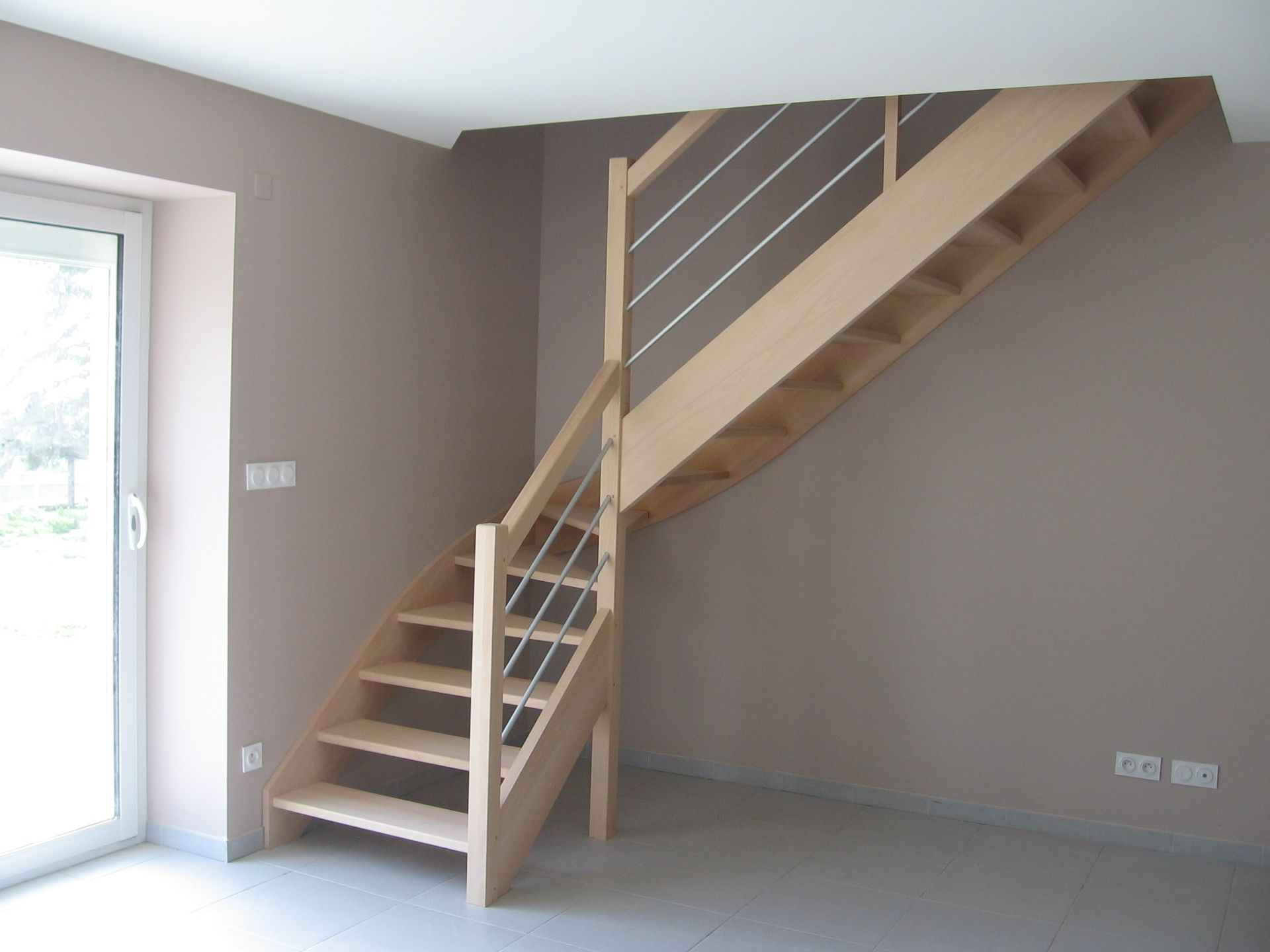 Escalier en bois avec contremarches ouvertes, rampe en bois clair et fins câbles métalliques dans une pièce moderne.