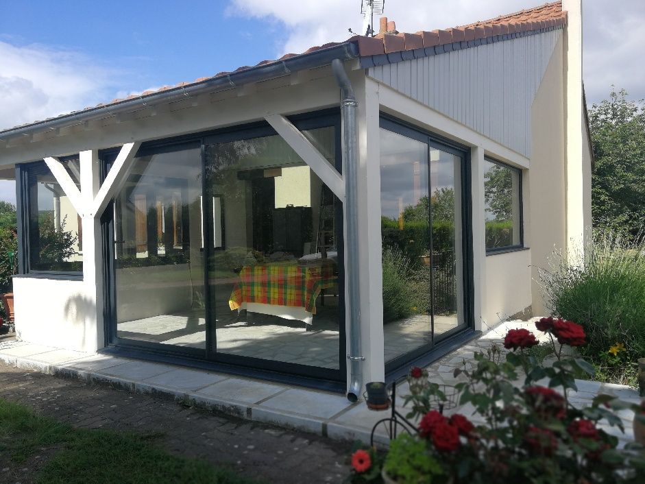 Extension de véranda avec de grandes portes coulissantes en verre, des poutres de soutien en bois et un rosier rouge au premier plan.