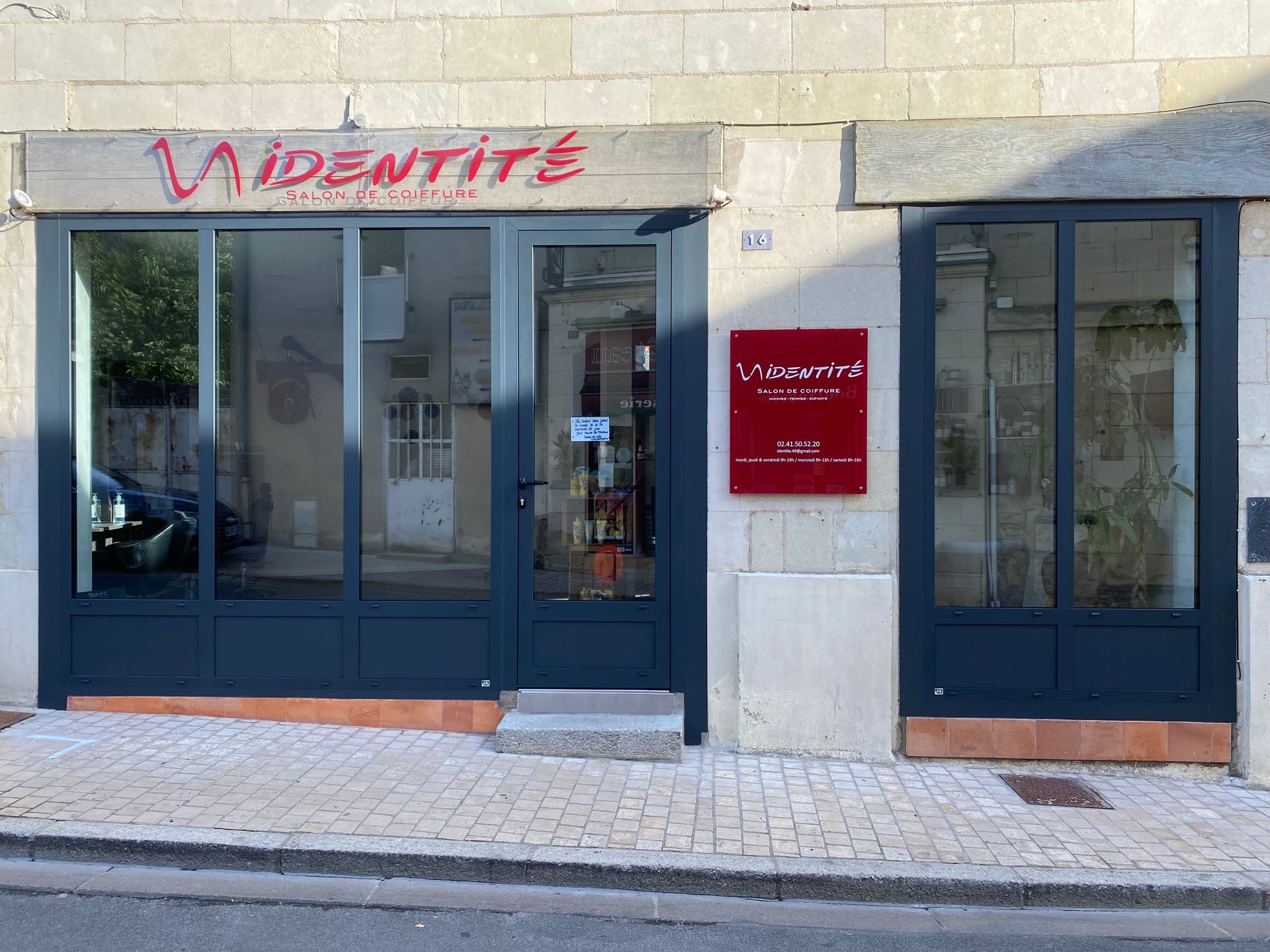 La façade d'un commerce nommé Identité, avec des cadres gris foncé, de grandes vitrines et une enseigne rouge sur un mur de pierre.
