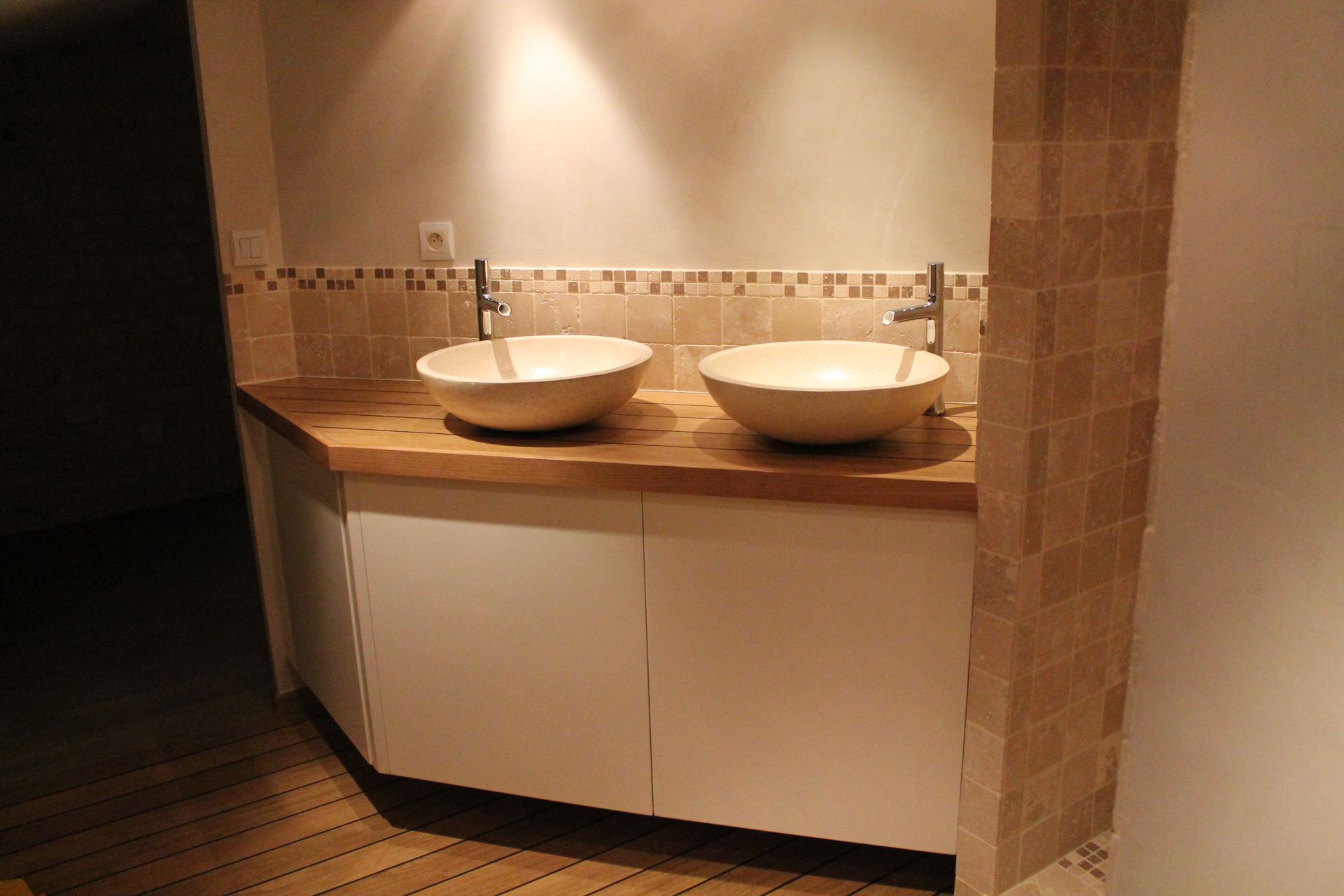 Un meuble-lavabo moderne avec deux vasques blanches sur un plan de travail en bois et des armoires blanches, le tout adossé à des murs carrelés.