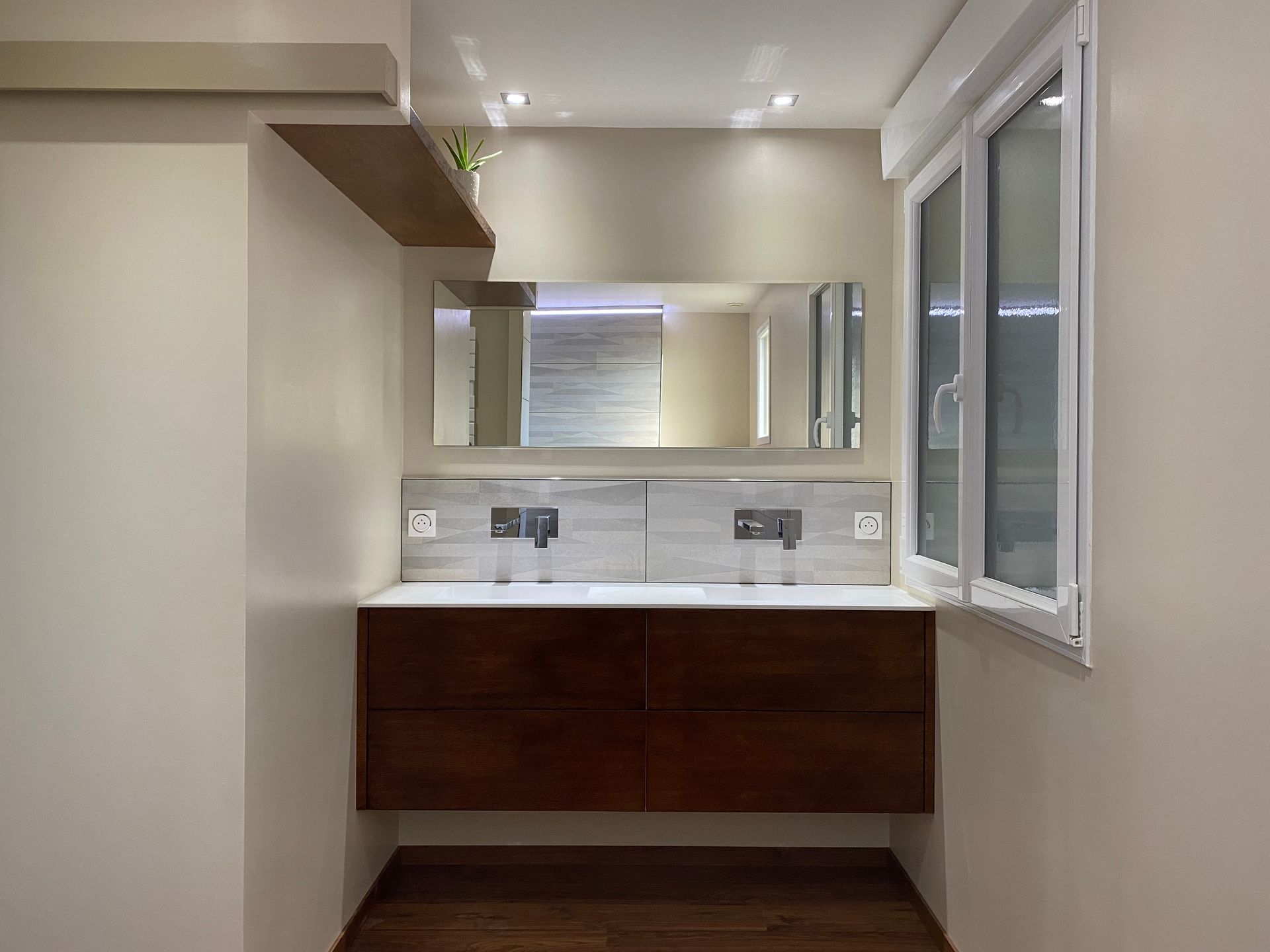 Un meuble-lavabo moderne avec un meuble en bois foncé, un plan de travail blanc, deux vasques, des robinets muraux et un grand miroir.