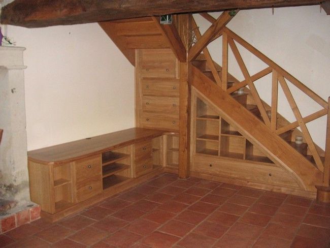 Escalier en bois avec étagères intégrées en dessous, adjacent à une armoire en bois assortie dans une pièce au sol carrelé.