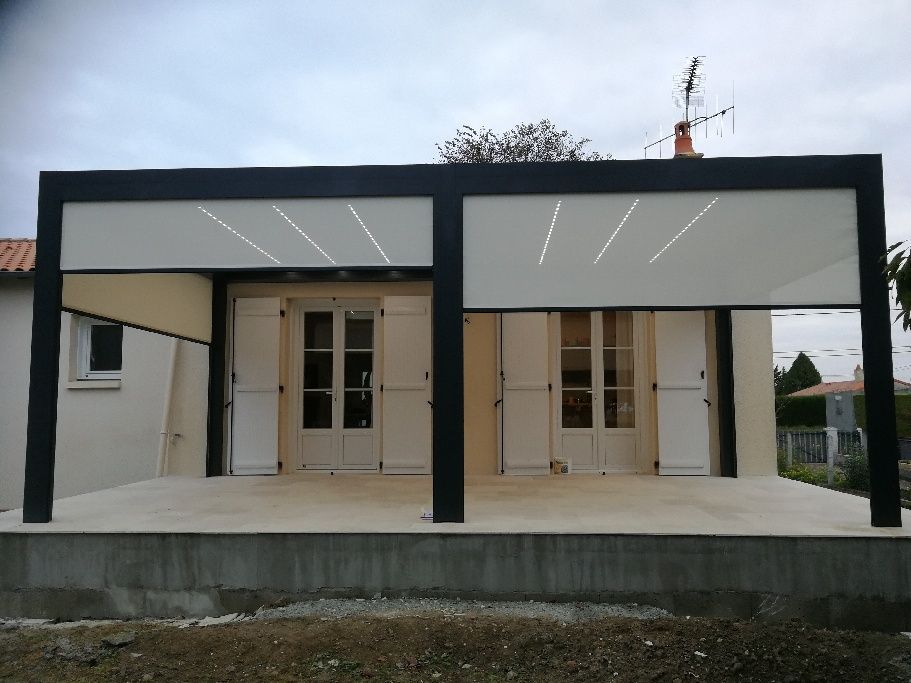 Une pergola de patio moderne à structure noire, avec éclairage intégré au plafond et écrans d'intimité abaissés, adossée à la façade d'une maison.