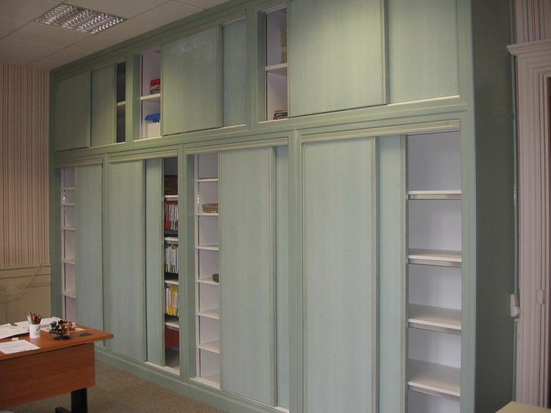 Un grand meuble mural vert clair avec des étagères allant du sol au plafond et des portes coulissantes, dans un environnement de bureau.