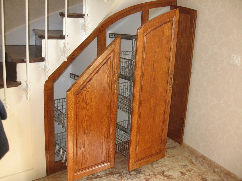 Meuble de rangement sous escalier avec portes en bois ouvertes révélant des étagères coulissantes en fil métallique.