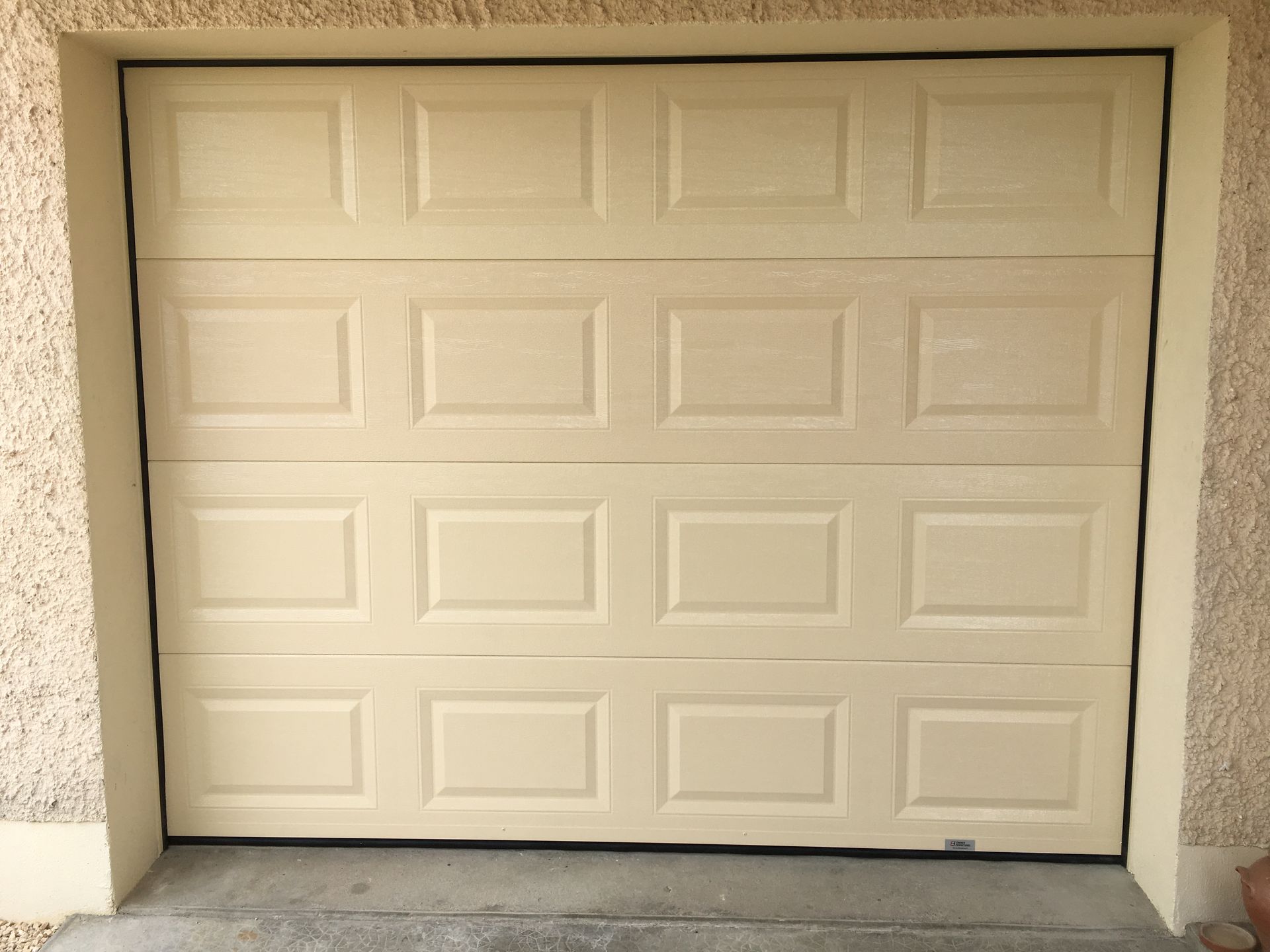 Une porte de garage résidentielle fermée, à quatre panneaux, de couleur beige clair, encadrée par des murs en stuc.